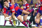Andrew Johns passes in a tackle.